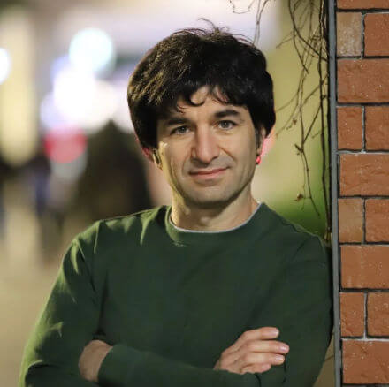 Head shot of John smiling, leaning against a brick wall